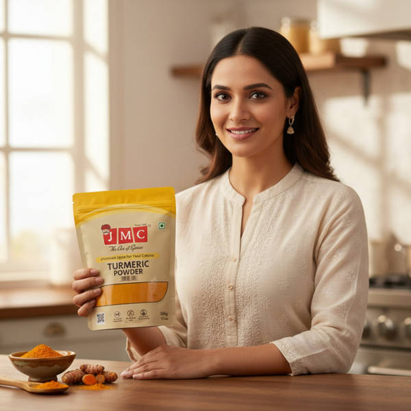 Woman Holding JMC Premium Haldi Turmeric Powder Pack in Kitchen with Fresh Turmeric Roots